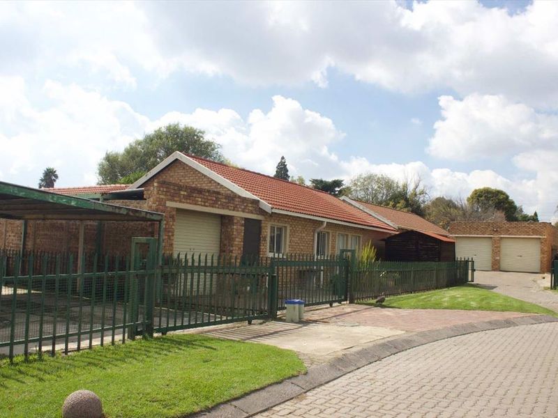 Front exterior view of a face brick house featuring a tiled roof, paved driveway, carport, and secure metal perimeter fencing.