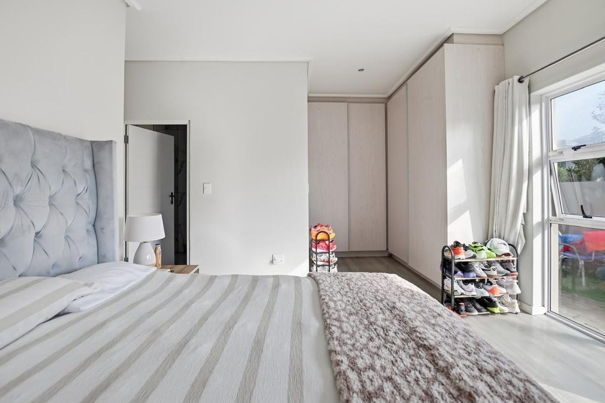A bright and modern bedroom featuring neutral tones, built-in floor-to-ceiling cupboards, and a large sliding glass door providing natural light and garden access.