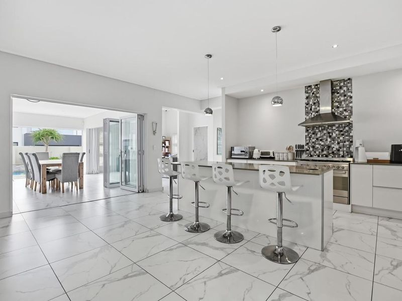 Modern open-plan kitchen and living area featuring a central island, marble-look floor tiles, and seamless indoor-outdoor flow through large bi-fold doors.