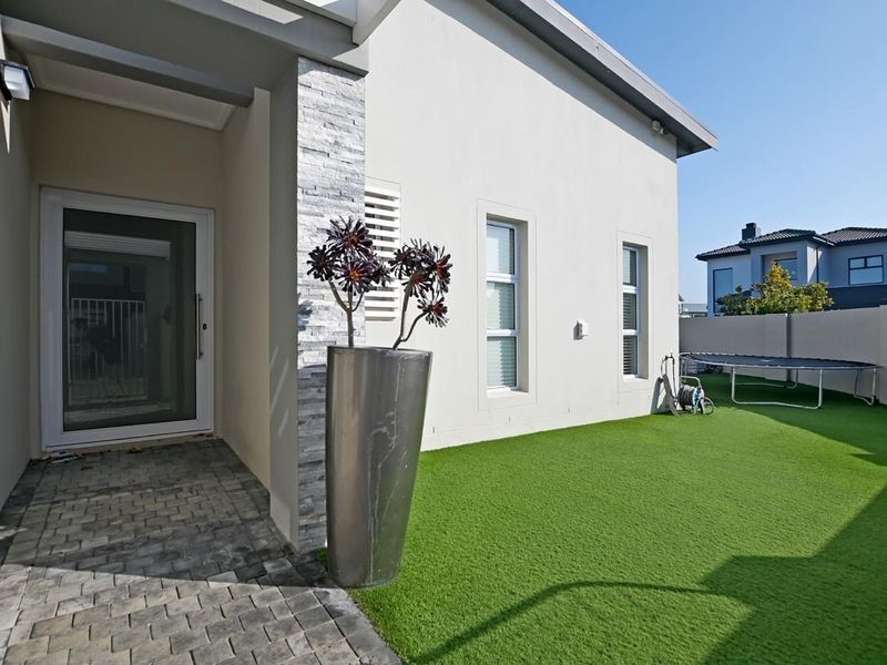 A well-maintained rear exterior area featuring a paved walkway, artificial lawn, and stone-clad architectural detailing on the building facade.