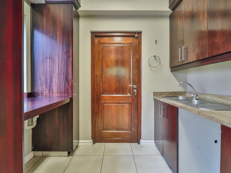A functional scullery area featuring dark wood cabinetry, stone countertops, a stainless steel sink, and tiled flooring, providing practical utility space.