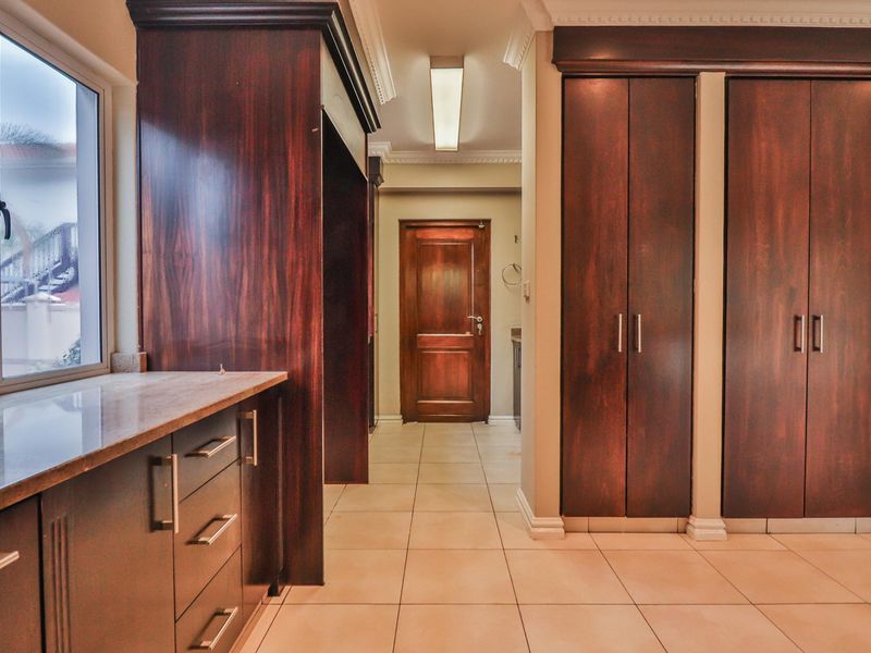 A well-maintained hallway featuring dark wood built-in cabinetry, tiled flooring, and classic crown molding, leading to a solid wood interior door.