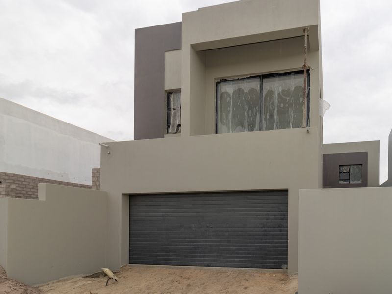 Modern two-story residential facade featuring a secure automated garage door and an upper-level balcony with sliding glass doors, currently in the final stages of construction.