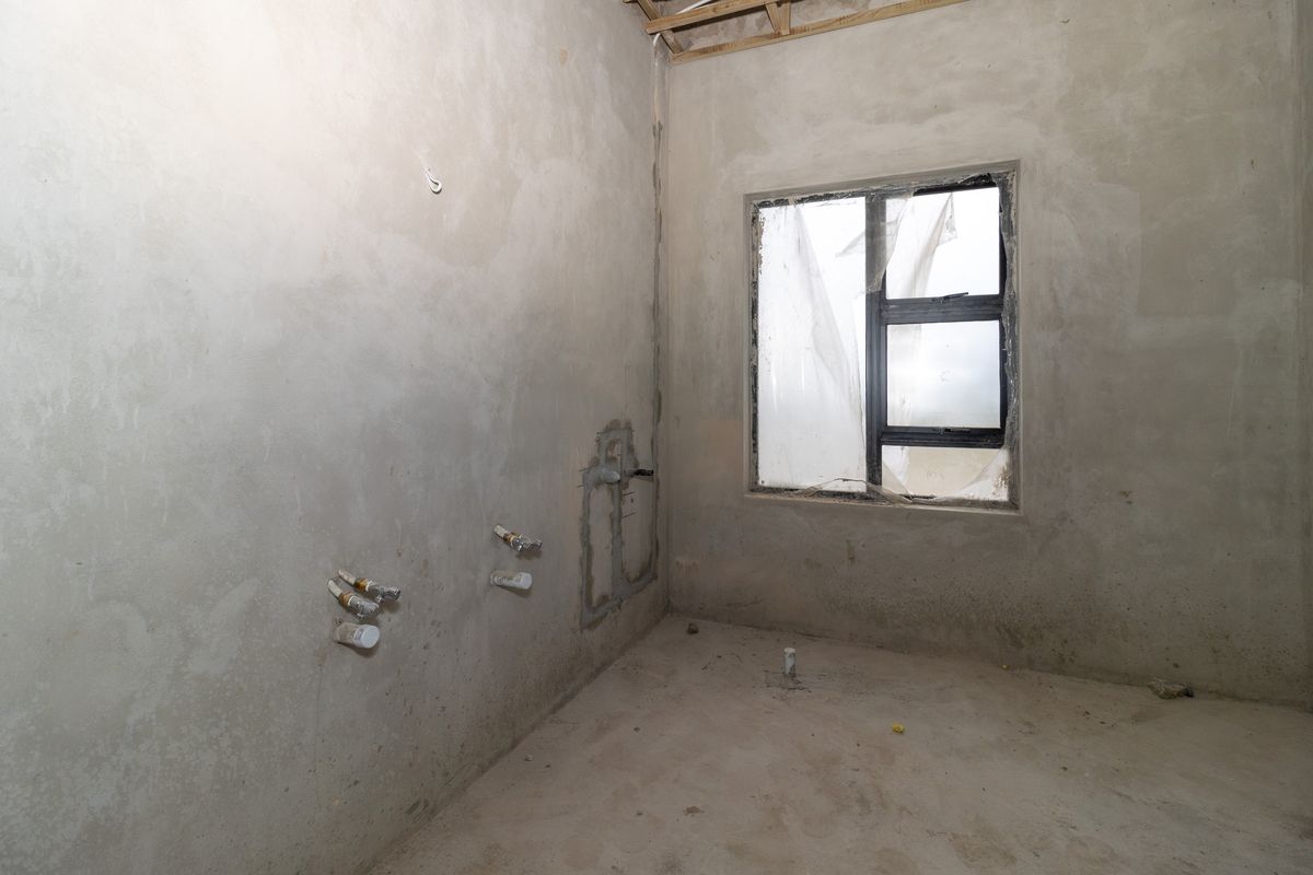 An unfinished kitchen space in shell condition, featuring exposed plumbing rough-ins and an installed aluminium window frame, ready for final finishes and cabinetry installation.