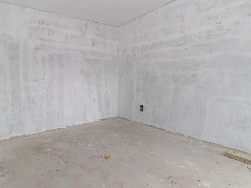 An empty, unfinished bedroom space featuring raw concrete flooring and unpainted plastered walls, ready for final interior finishes and flooring installation.