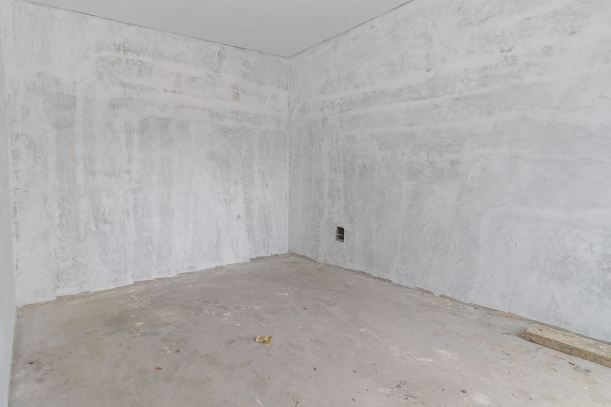 An empty, unfinished bedroom space featuring raw concrete flooring and unpainted plastered walls, ready for final interior finishes and flooring installation.