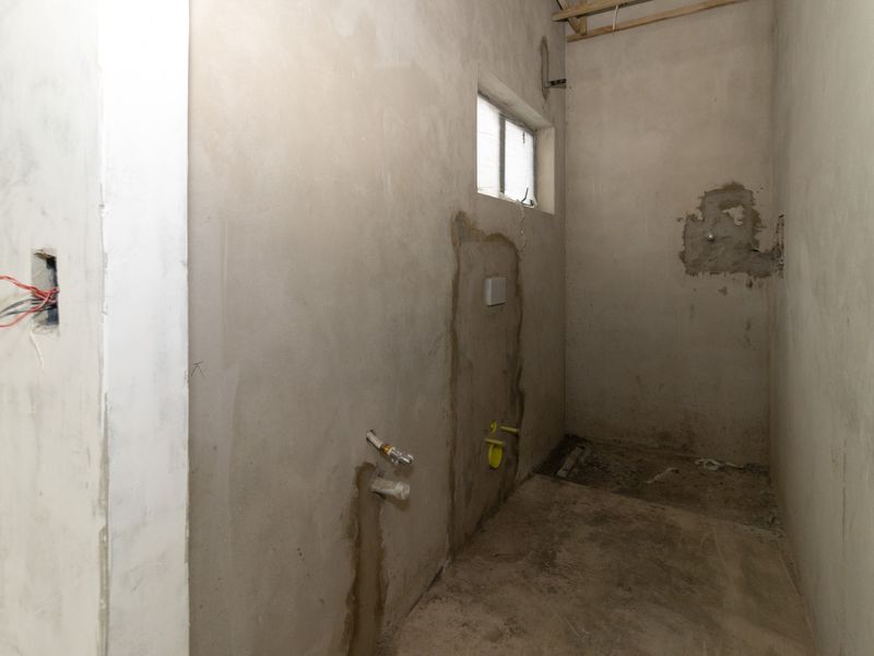An unfinished bathroom space in shell condition, featuring exposed plumbing rough-ins, electrical wiring, and raw plaster walls, ready for final fit-out and finishes.