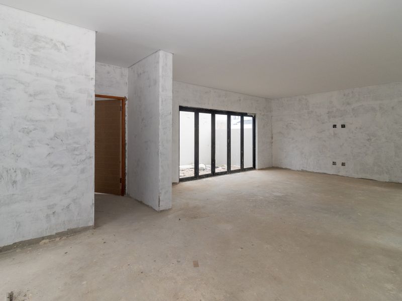 An expansive, unfinished open-plan living area featuring raw plaster walls, concrete flooring, and modern black aluminium stacker doors leading to the exterior.