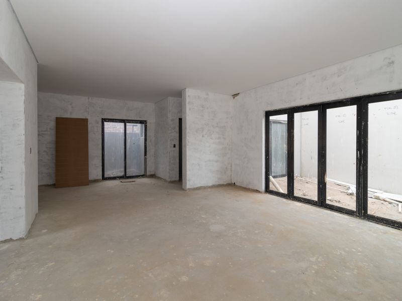 An unfinished open-plan living area featuring concrete flooring, plastered walls, and large black aluminium sliding doors leading to an outdoor space.