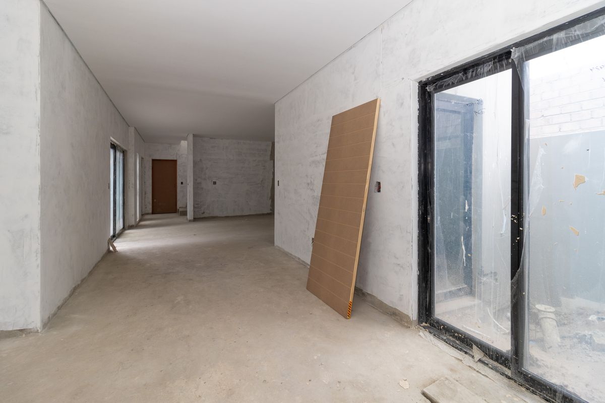 An unfinished interior living space featuring concrete flooring, plastered walls, and large sliding glass doors, currently in a shell construction state.