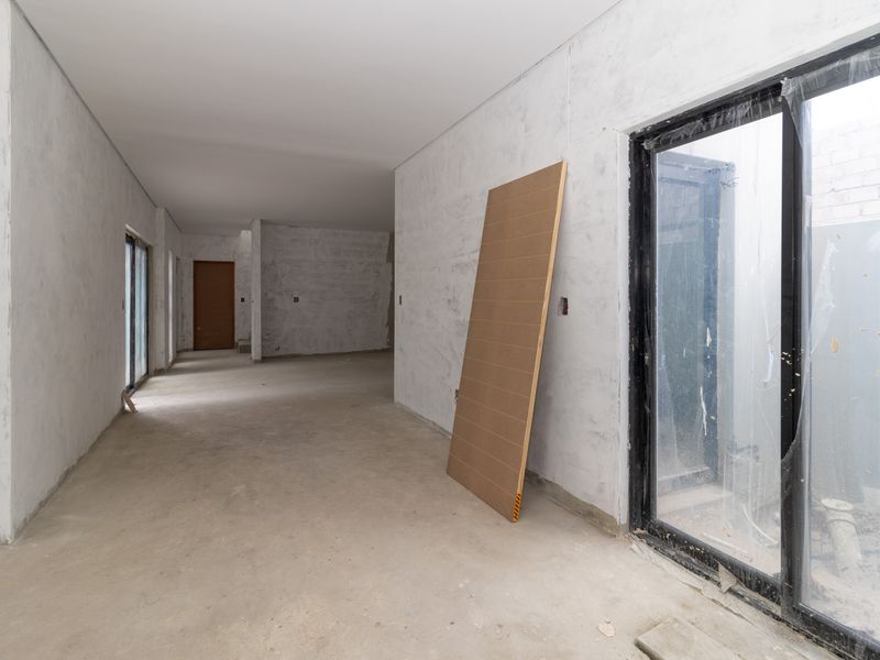 An unfinished interior living space featuring concrete flooring, plastered walls, and large sliding glass doors, currently in a shell construction state.