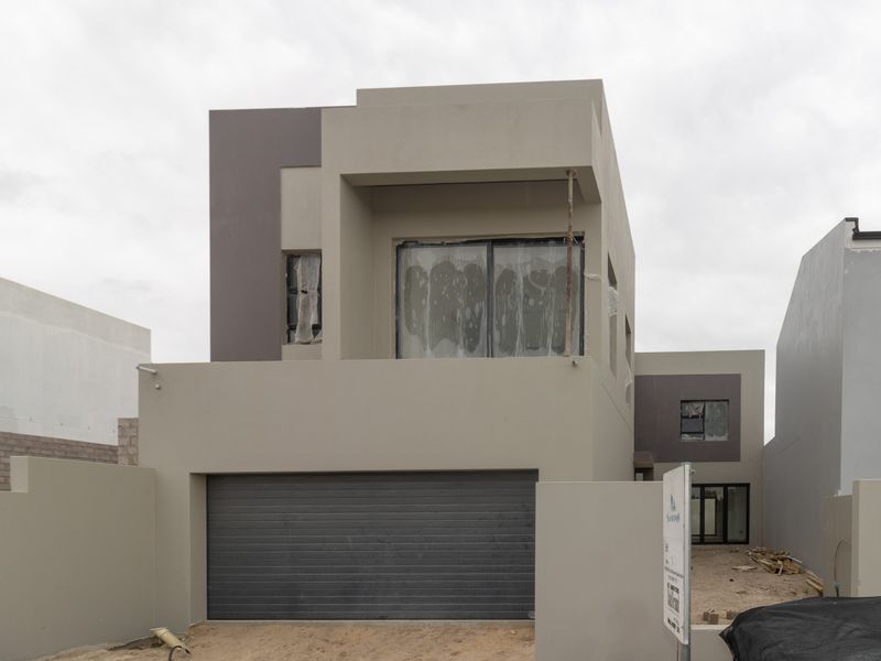 Modern double-story residential property under construction, featuring a roller garage door, balcony, and contemporary plastered facade.