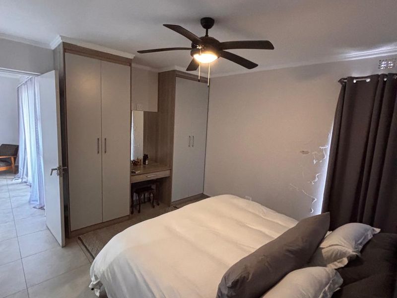 A bedroom featuring built-in cupboards with an integrated vanity, a ceiling fan, and tiled flooring.