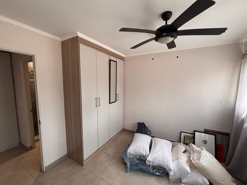 A clean bedroom featuring neutral tiled flooring, a modern ceiling fan, and a large built-in wardrobe with light wood-tone accents.