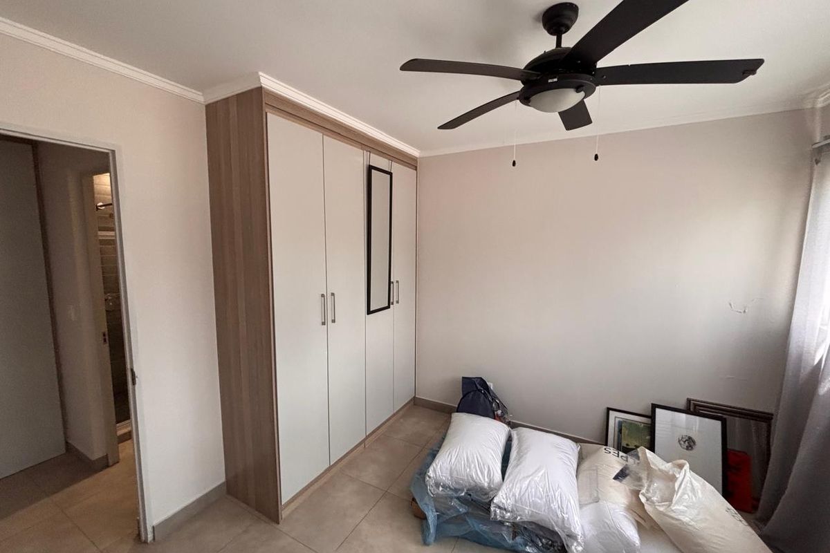A clean bedroom featuring neutral tiled flooring, a modern ceiling fan, and a large built-in wardrobe with light wood-tone accents.