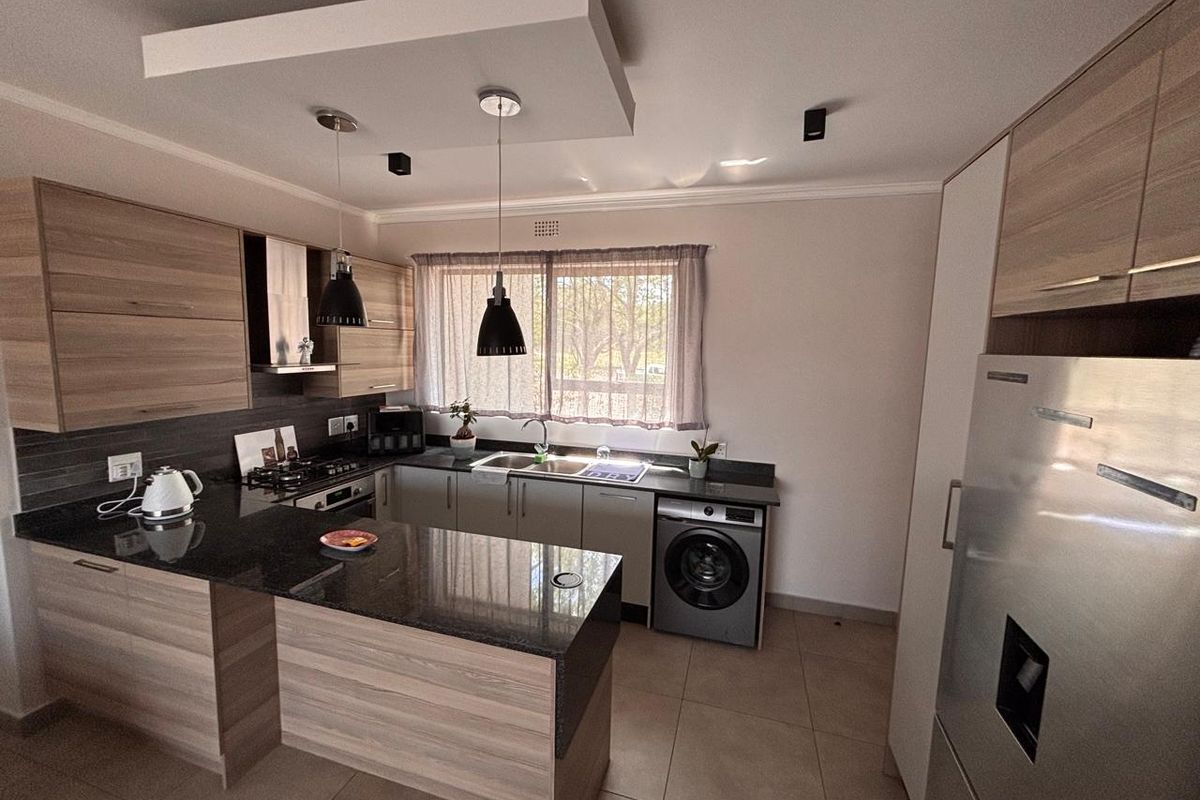Modern kitchen featuring wood-finish cabinetry, granite countertops, integrated appliances, and a functional layout with a breakfast bar and recessed ceiling lighting.