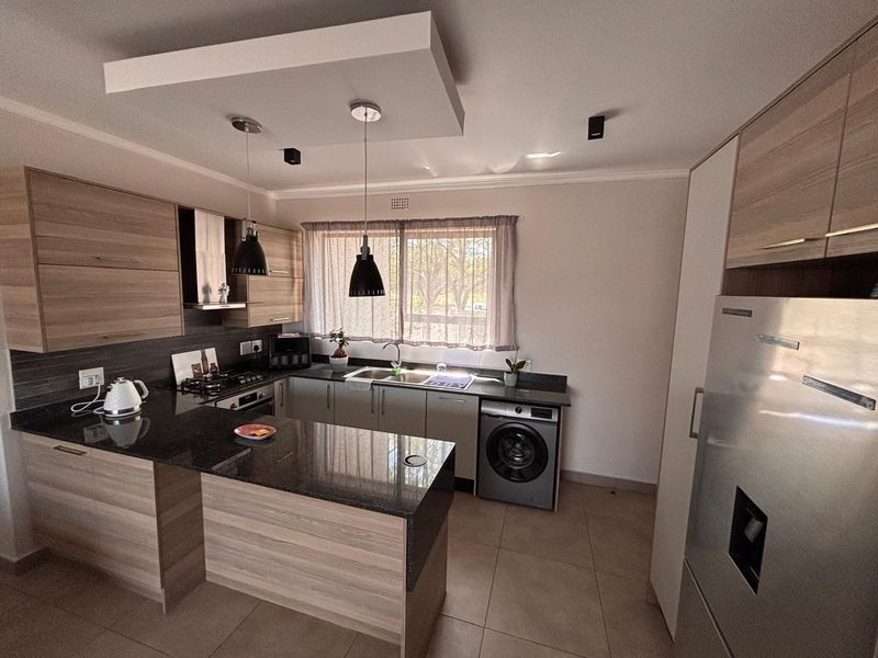 Modern kitchen featuring wood-finish cabinetry, granite countertops, integrated appliances, and a functional layout with a breakfast bar and recessed ceiling lighting.