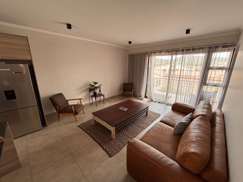 A bright open-plan living area featuring neutral tiled flooring, modern recessed lighting, and large sliding glass doors leading to a balcony.