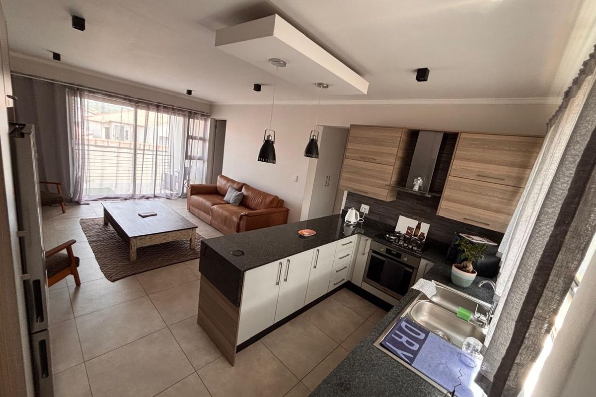 Modern open-plan living area featuring a contemporary kitchen with granite countertops, built-in appliances, and seamless flow to a bright lounge with sliding door access.