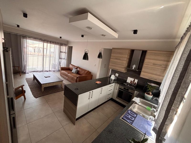 Modern open-plan living area featuring a contemporary kitchen with granite countertops, built-in appliances, and seamless flow to a bright lounge with sliding door access.