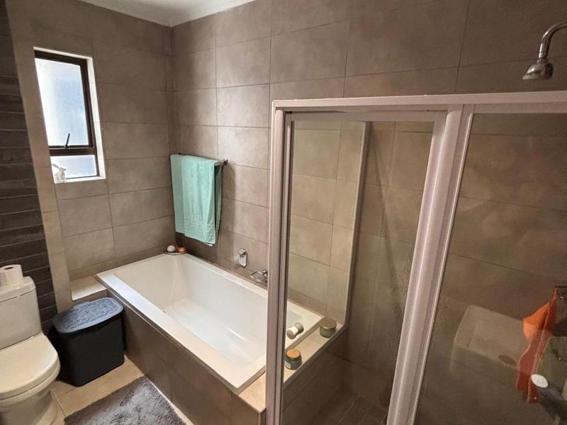 A well-maintained bathroom featuring a built-in bathtub, separate glass shower enclosure, toilet, and neutral tiled finishes.