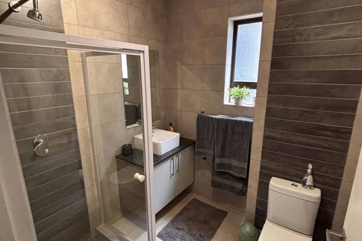 Modern bathroom featuring a glass shower enclosure, vanity cabinet with vessel sink, and neutral-toned wall and floor tiling.