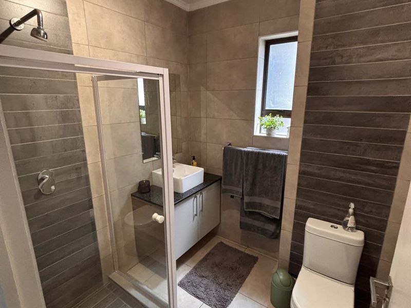 Modern bathroom featuring a glass shower enclosure, vanity cabinet with vessel sink, and neutral-toned wall and floor tiling.
