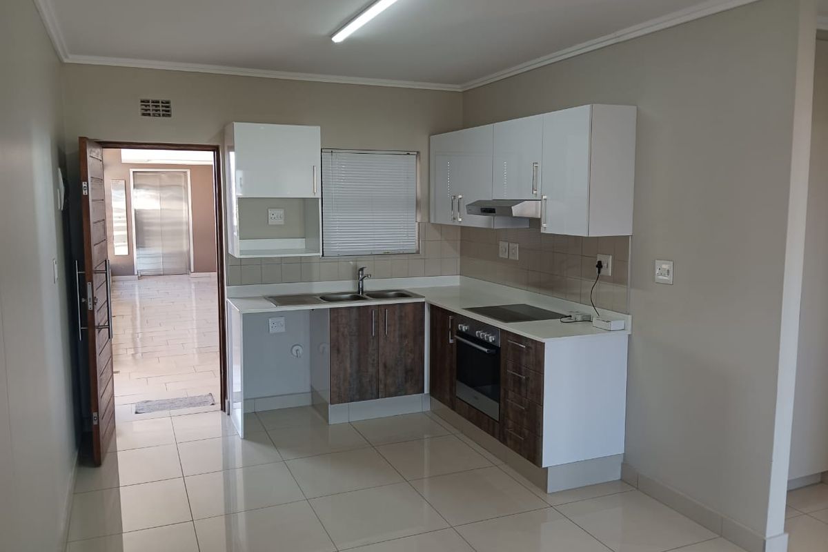 Modern kitchen featuring white and wood-tone cabinetry, integrated oven and hob, tiled flooring, and a clean, functional layout.