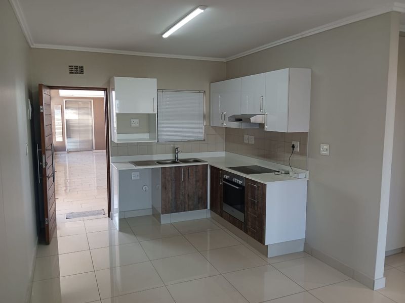 Modern kitchen featuring white and wood-tone cabinetry, integrated oven and hob, tiled flooring, and a clean, functional layout.