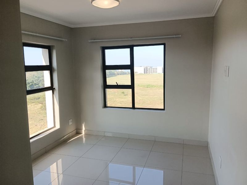 A bright, empty bedroom featuring neutral tiled flooring, modern aluminium window frames, and clean finishes, offering a blank canvas for personalization.