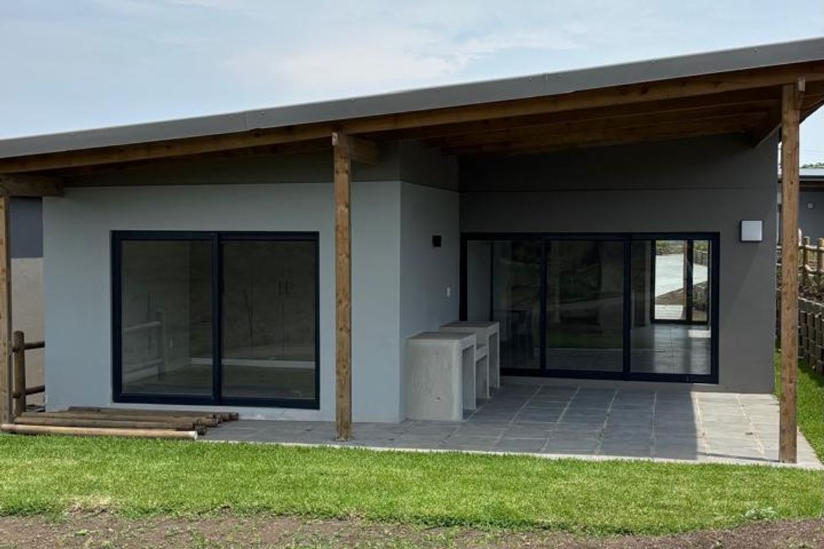 Rear view of a modern home featuring a covered patio with a built-in braai, sliding glass doors, and timber structural supports.