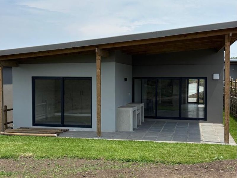 Rear view of a modern home featuring a covered patio with a built-in braai, sliding glass doors, and timber structural supports.