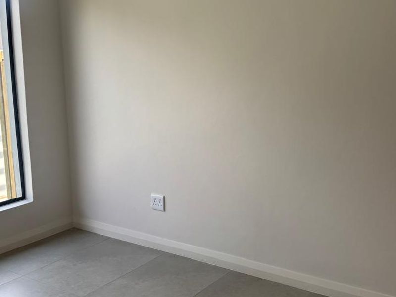 A clean, empty bedroom featuring neutral tiled flooring, modern skirting boards, and a large window, providing a blank canvas for interior design.