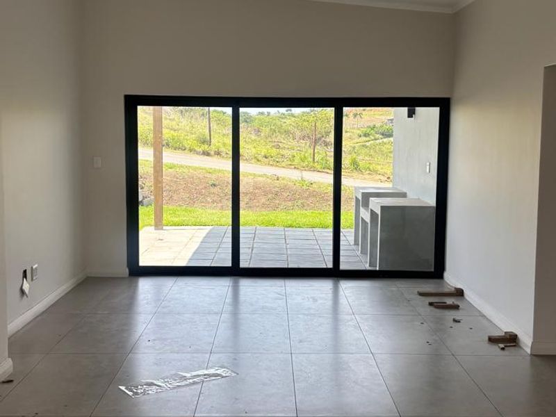 An empty, open-plan living area featuring large sliding glass doors that provide natural light and access to an outdoor patio space.