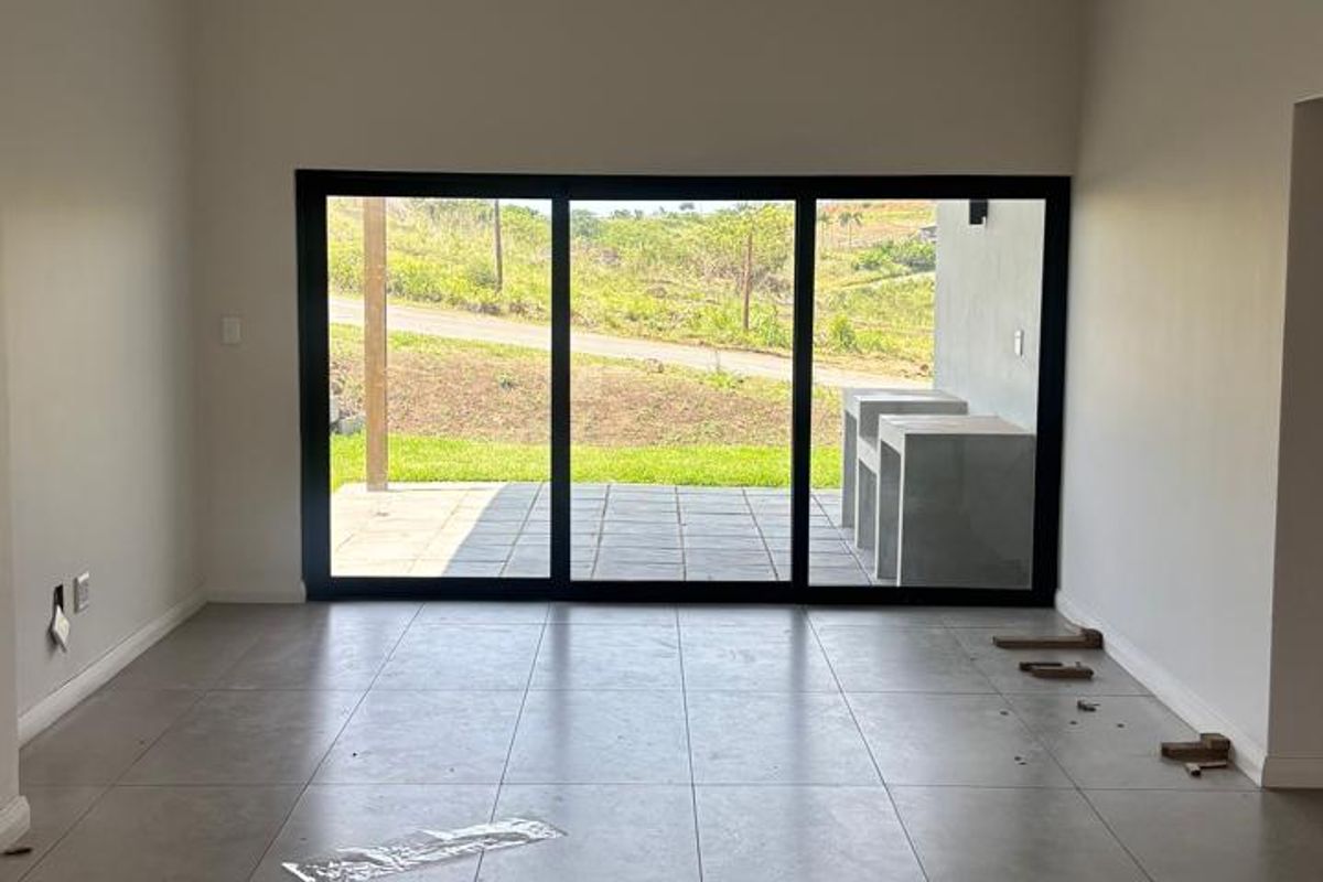 An empty, open-plan living area featuring large sliding glass doors that provide natural light and access to an outdoor patio space.