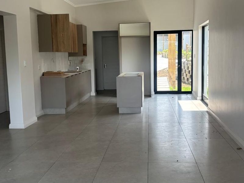 An open-plan living and kitchen area featuring large format floor tiles, recessed lighting, and unfinished cabinetry awaiting final installation and countertops.