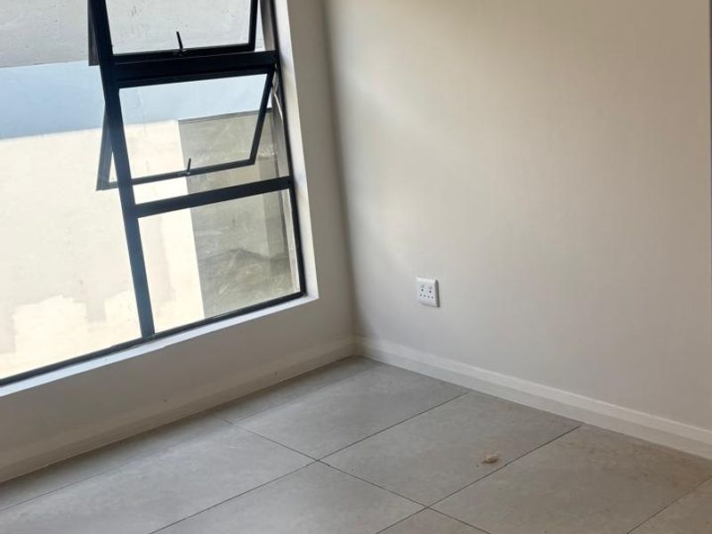 A bright, empty bedroom featuring large format floor tiles, neutral walls, and a modern aluminium window frame.