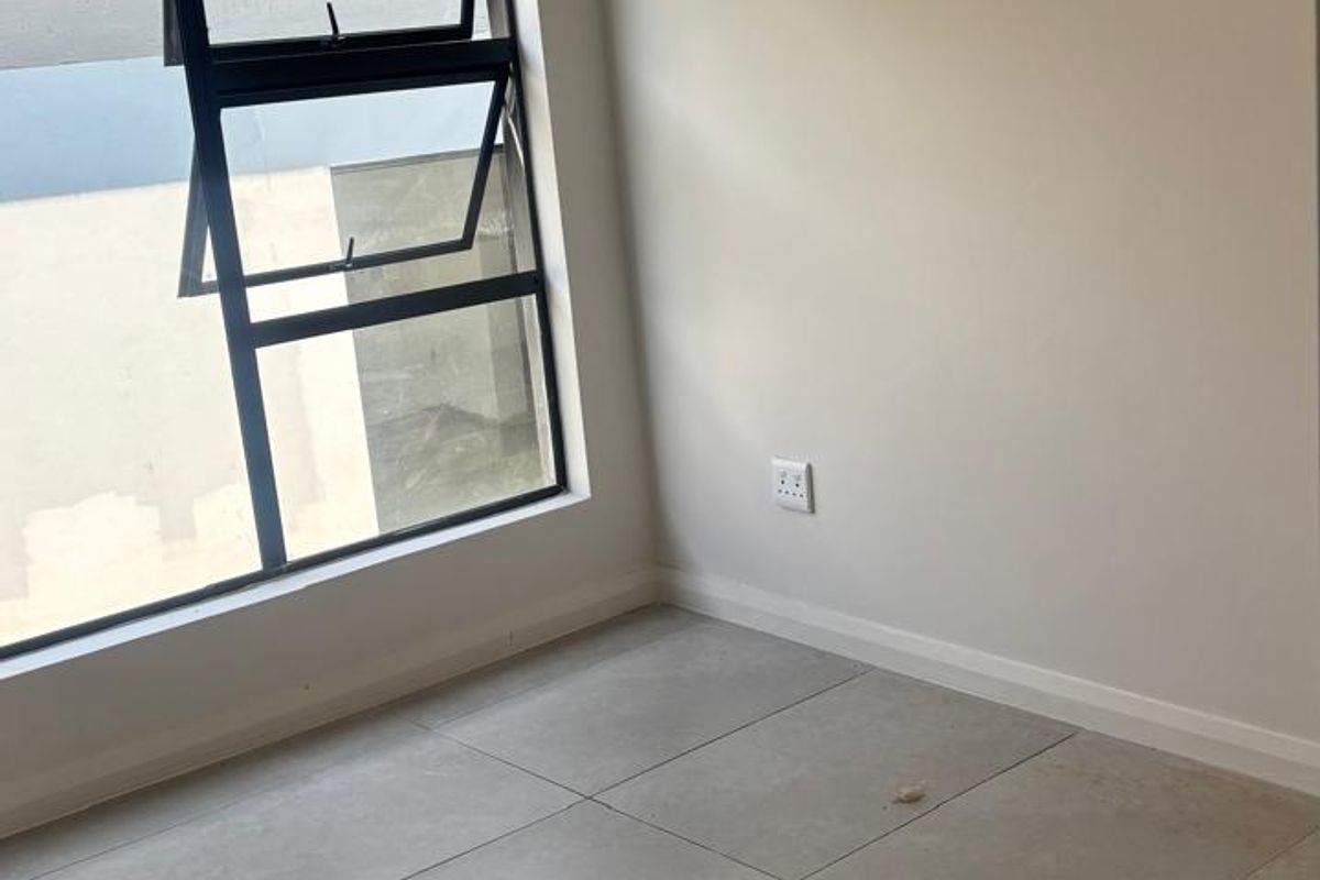 A bright, empty bedroom featuring large format floor tiles, neutral walls, and a modern aluminium window frame.
