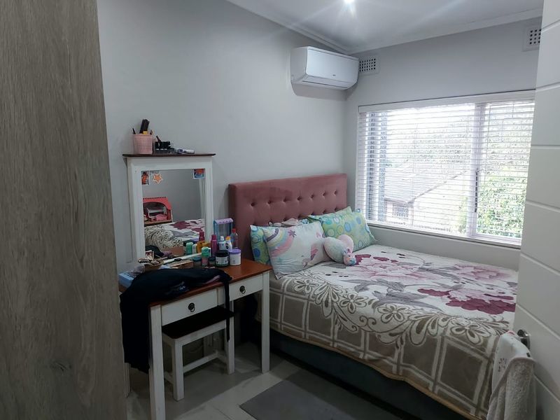A well-maintained bedroom featuring a split-system air conditioner, venetian blinds, and built-in storage, offering a comfortable and functional living space.