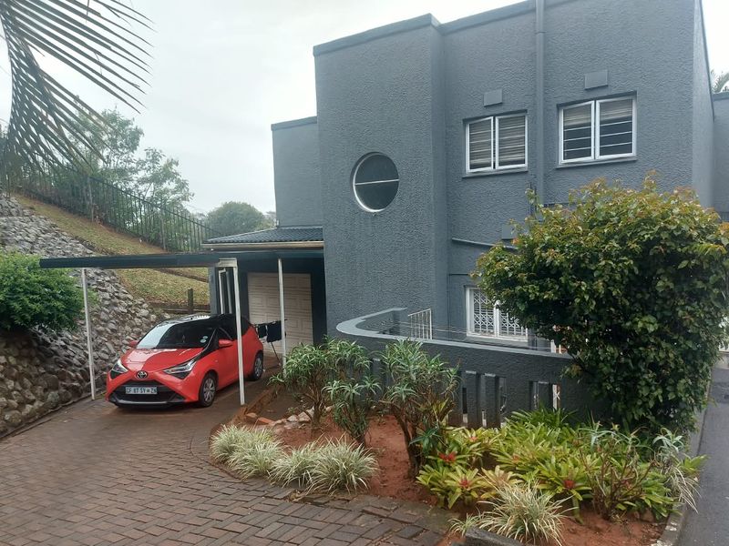 Front elevation of a modern apartment building featuring a paved driveway, integrated carport, garage, and landscaped garden area with security features.
