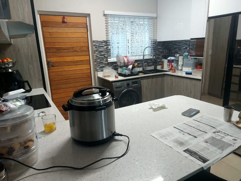 Modern kitchen featuring quartz countertops, mosaic tile backsplash, built-in cabinetry, and an integrated washing machine, offering a functional and contemporary workspace.