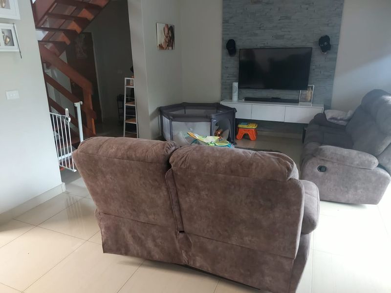 A comfortable living room featuring a stone accent wall, floating media console, and an open wooden staircase leading to the upper level.