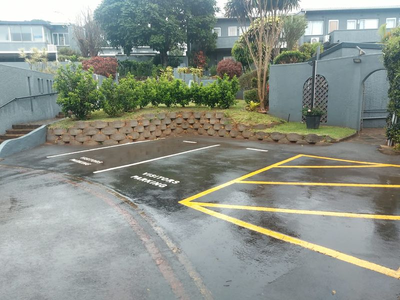 A paved visitors parking area featuring a retaining wall, landscaped garden beds, and painted masonry boundary walls within an apartment complex.