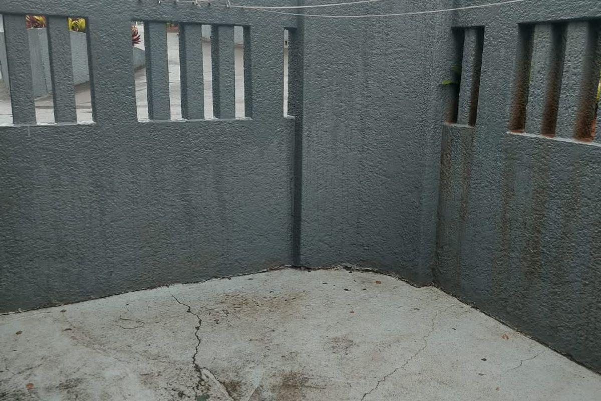 A private rear courtyard area featuring a textured concrete boundary wall and paved flooring with visible surface cracking and weathering.