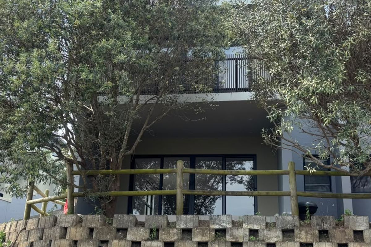 Rear view of the townhouse featuring a tiered concrete block retaining wall, timber fencing, and a balcony overlooking the lower level sliding glass doors.