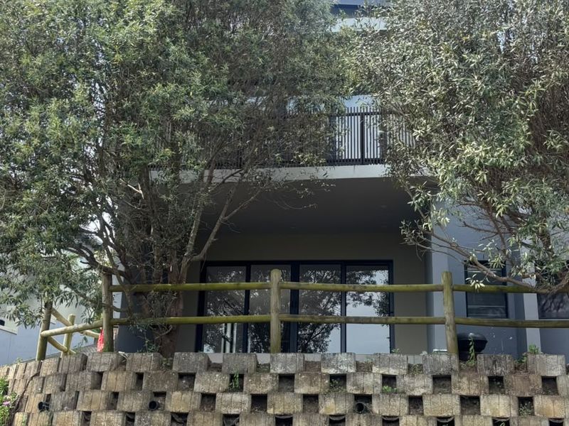 Rear view of the townhouse featuring a tiered concrete block retaining wall, timber fencing, and a balcony overlooking the lower level sliding glass doors.
