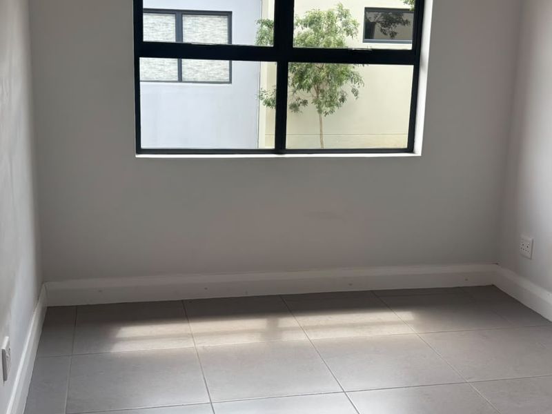 A bright, empty bedroom featuring neutral tiled flooring, modern black-framed windows, and recessed downlighting, providing a clean canvas for personalization.