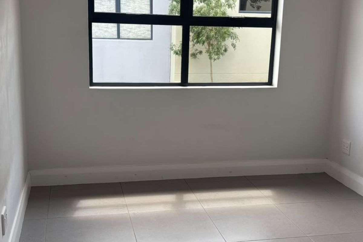 A bright, empty bedroom featuring neutral tiled flooring, modern black-framed windows, and recessed downlighting, providing a clean canvas for personalization.