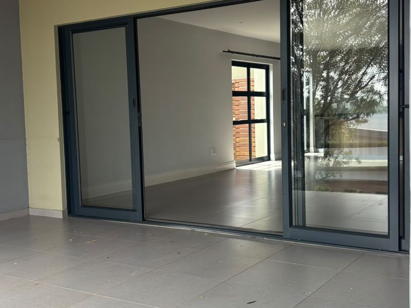A covered patio area featuring large sliding glass doors that open into an empty interior living space with modern tiled flooring.