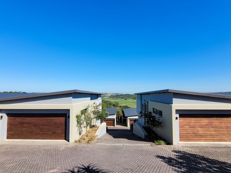 Front view of modern townhouse units featuring timber-look garage doors, paved driveway, and contemporary architectural design with scenic landscape views.